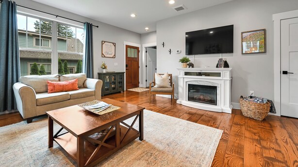 A living room with a sofa, coffee table, fireplace, TV, and a view of the outside.