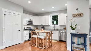 A modern kitchen with white cabinets, a wooden table, and a blue side table with books.