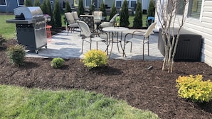 Un patio con una parrilla, mobiliario exterior y un pequeño jardín.