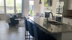 Una cocina moderna con encimera de mármol, taburetes de bar y un comedor con una silla blanca.