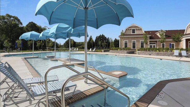 Una piscina con varias sombrillas, sillas de descanso y un edificio al fondo.