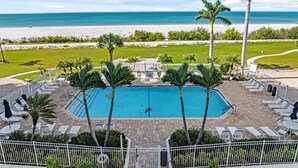 A pool area with lounge chairs and palm trees, overlooking a beach. - Ocean Views From Every Window | Condo 206C at Estero Beach & Tennis Club + 2 Bikes, Beach Gear. 6-7night stays (Fort Myers Beach)