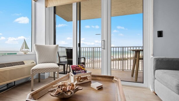 A modern living room with a view of the beach, a chair, a table with a magazine, and a small sofa. - Ocean Views From Every Window | Condo 206C at Estero Beach & Tennis Club + 2 Bikes, Beach Gear. 6-7night stays (Fort Myers Beach)