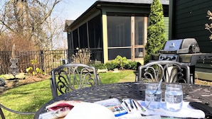 Een terras buiten met een eettafel, inclusief een barbecue en uitzicht op een huis.