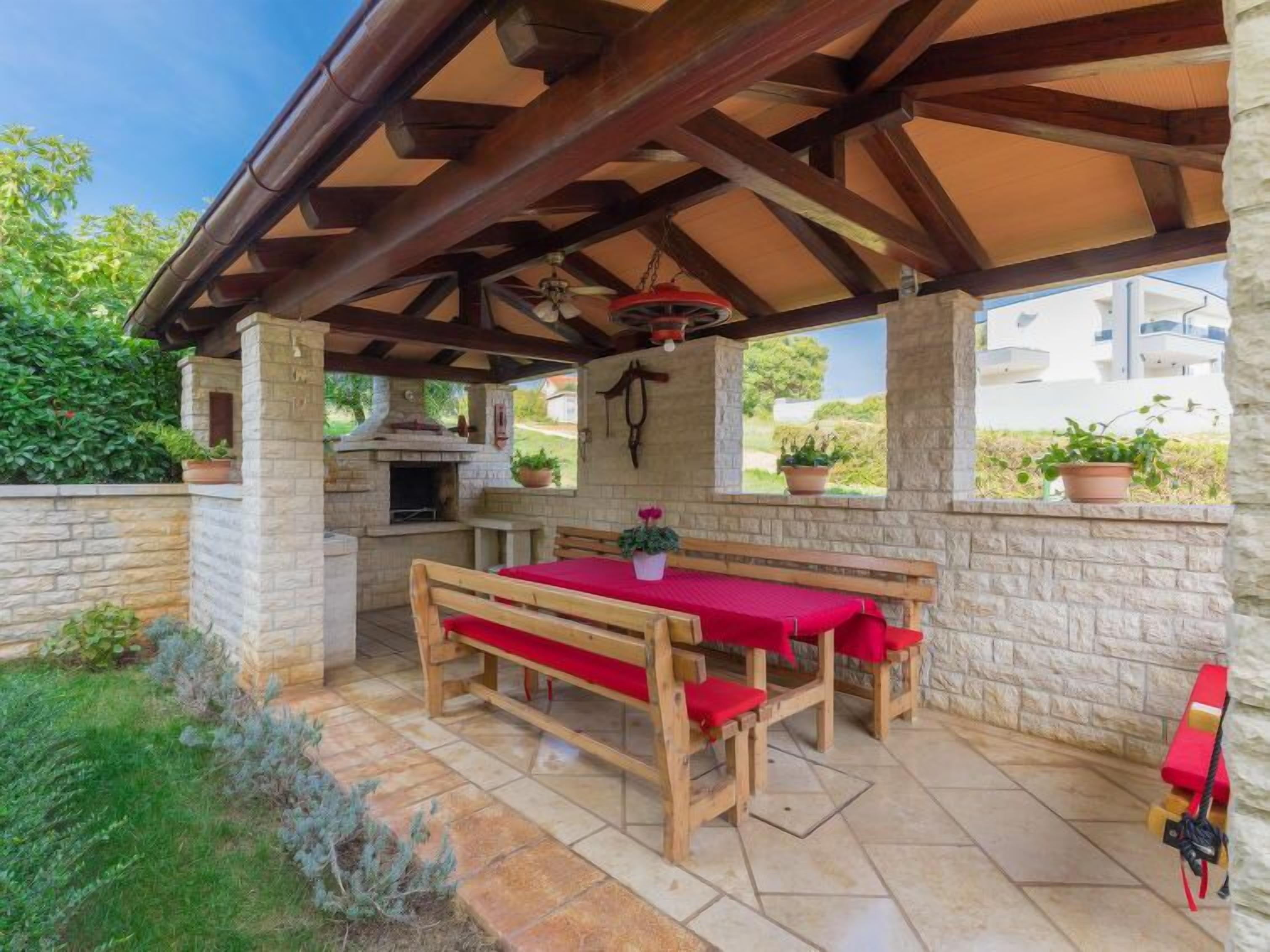 An outdoor patio with a stone wall, a wooden table with red cushions, a stone bench, and a hanging light fixture.