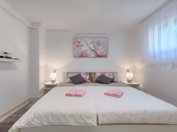 A double room with two beds, each with a white bedspread and pink towels. There is a large floral artwork on the wall above the beds, and two bedside lamps.