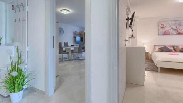 Un salon moderne avec un canapé blanc, un coin repas avec une table et des chaises, et une cuisine visible au fond.