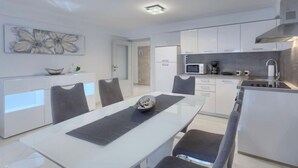 Une cuisine moderne avec des meubles blancs, une table à manger avec des chaises et un four à micro-ondes.