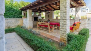 Une terrasse extérieure avec des piliers en pierre, un banc en bois, une balançoire et un barbecue.