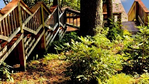 A wooden deck with a staircase leading to a dock extending over water, surrounded by lush greenery.