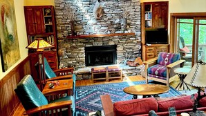 A cozy living room with a stone fireplace, wooden furniture, and a view of the outdoors.