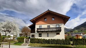 Un bâtiment à deux étages doté d’un balcon, entouré de verdure et avec des montagnes en arrière-plan.
