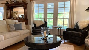 A living room with a glass coffee table, two black leather armchairs, a white sofa, and a large window with curtains. - Hidden Country Gem with Pond | Free Early In & Late Out | Pet Friendly! (Nevada City)