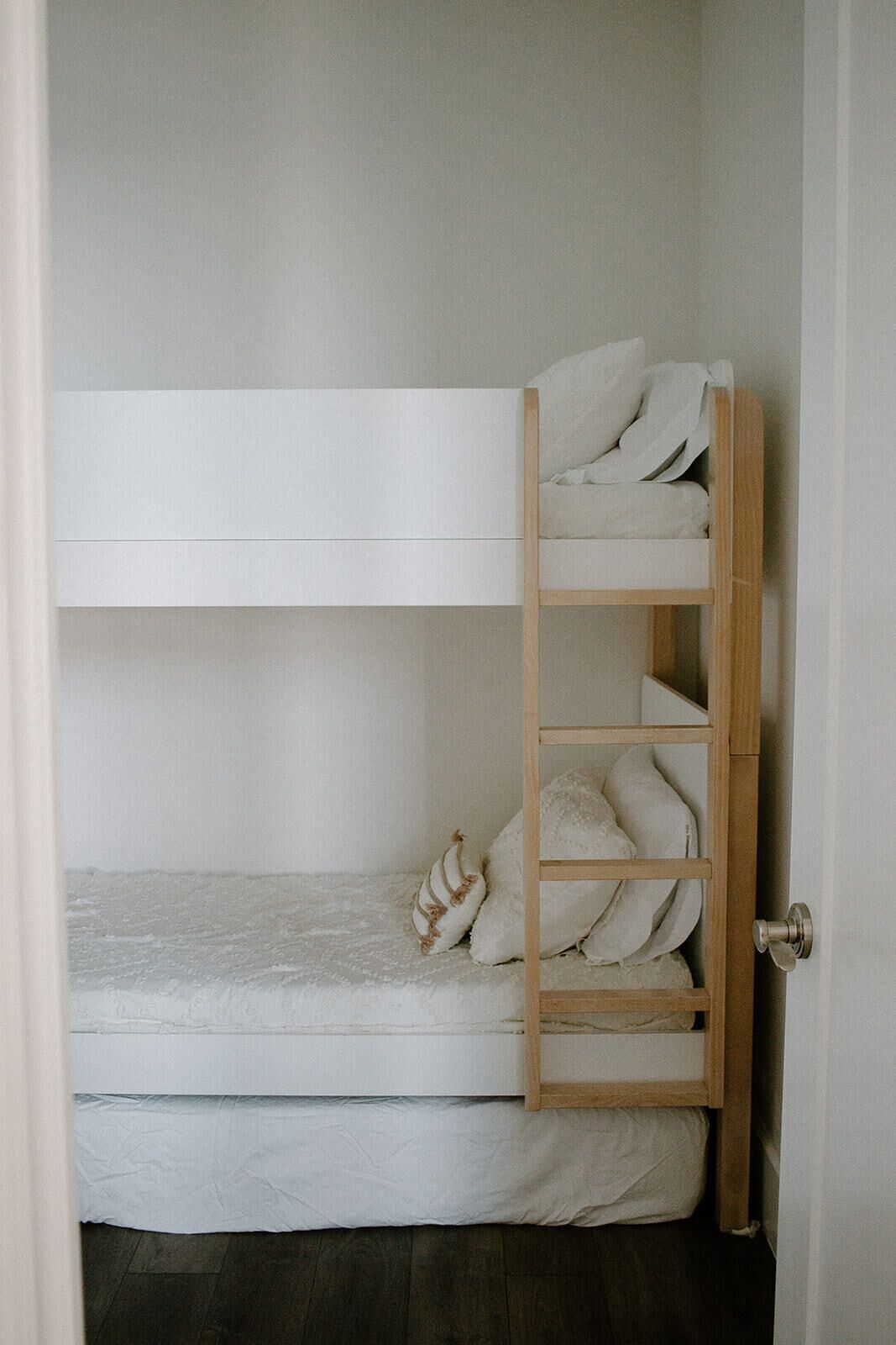 Un lit superposé avec une échelle en bois, du linge de lit blanc et une porte sur le côté droit.