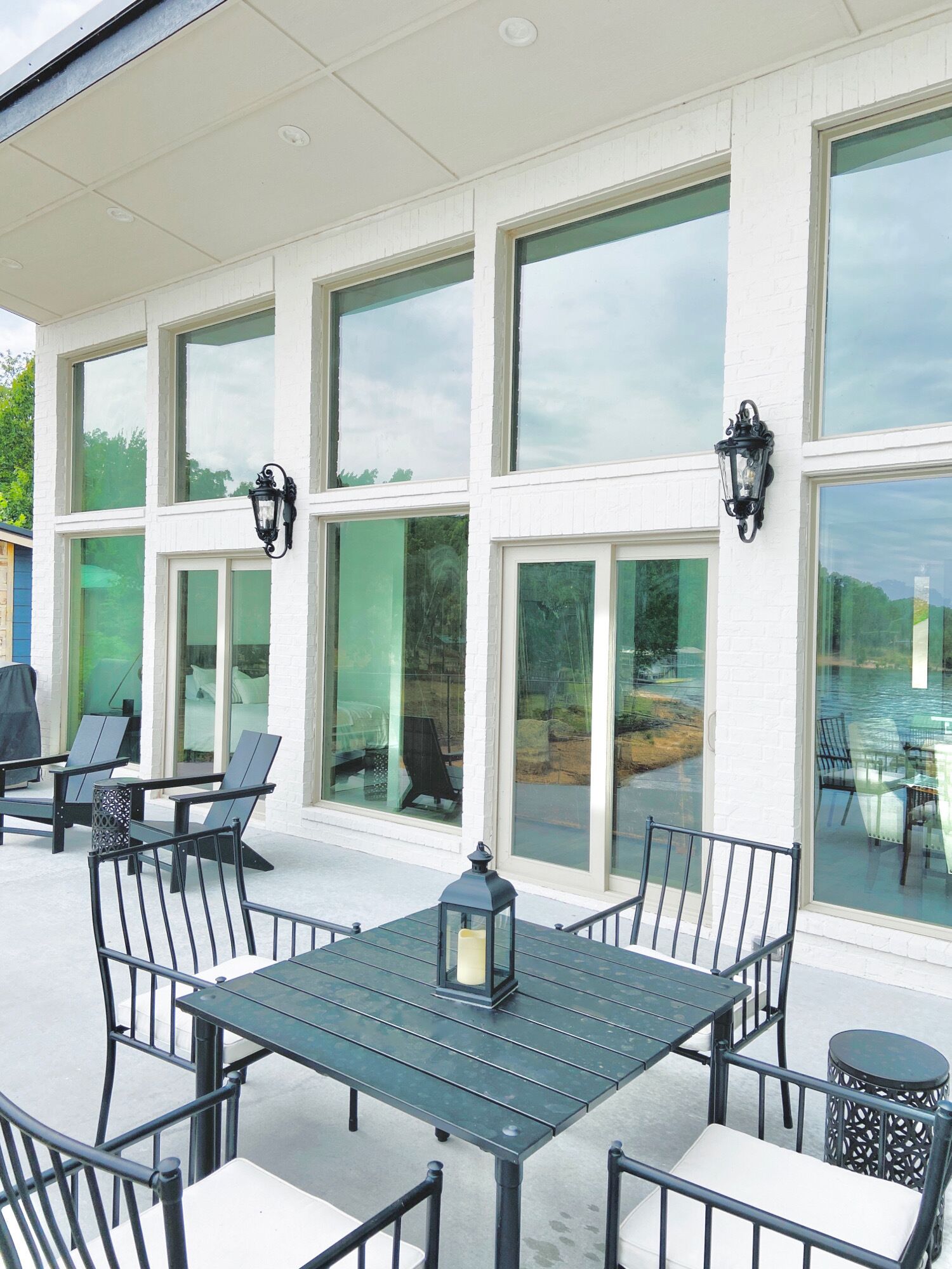 A covered outdoor seating area with a table and chairs, large windows, and outdoor lighting fixtures.