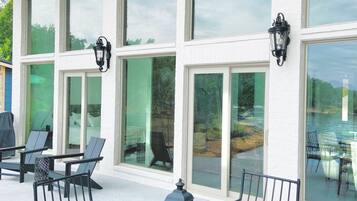 A covered outdoor seating area with a table and chairs, large windows, and outdoor lighting fixtures.
