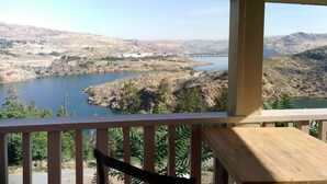 A view from a balcony overlooking a river, surrounded by hills and sparse vegetation.