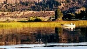 A calm river with a boat and a rocky cliff in the background.