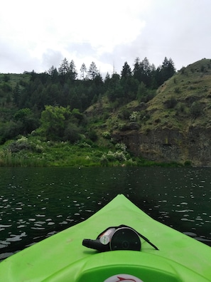 A green kayak on calm water with a forested hillside in the background.