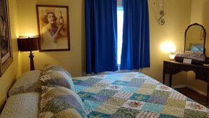 A bedroom with a bed, a nightstand, a mirror, and a window with blue curtains.