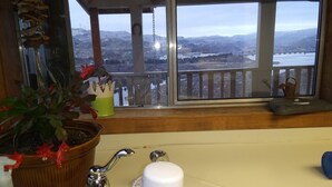 A bathroom with a bathtub, a sink with a faucet, and a window with a view of a river and mountains.