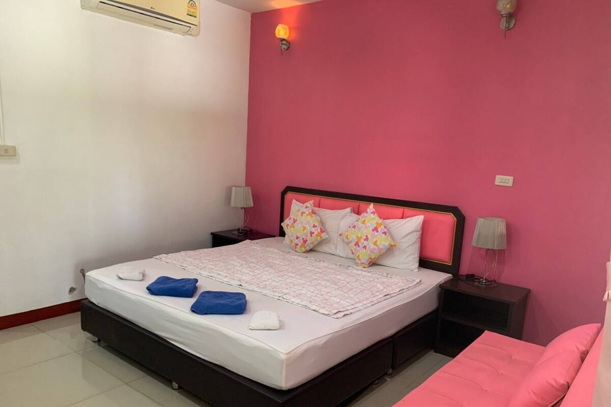 Un dormitorio con cama, dos mesitas de noche, una pared rosa y un sofá rosa.