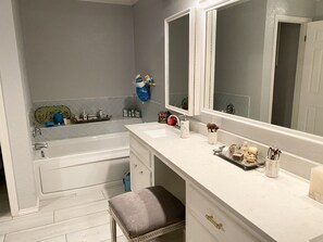 Bathroom features a large bathtub and a vanity area with a sink, mirror, and toiletries.