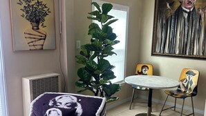 A room with a bed, a potted plant, a dining table with chairs, and a large painting on the wall. - Milano Art Studio Apartment (Los Angeles)
