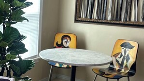A dining area with a round table, two chairs, a potted plant, and a large painting on the wall. - Milano Art Studio Apartment (Los Angeles)
