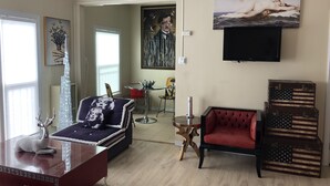 A living room with a red sofa, a blue sofa with a patterned cover, a wooden coffee table, and a decorative glass sculpture. There is a painting on the wall and a television mounted above it. - Milano Art Studio Apartment (Los Angeles)
