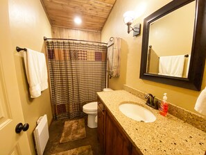A bathroom with a wooden ceiling, a white sink, a toilet, a shower curtain, and a mirror.