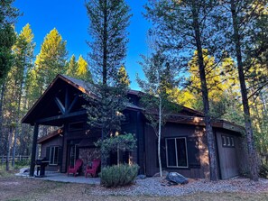 A cabin with a covered porch, two red Adirondack chairs, and a stone wall.