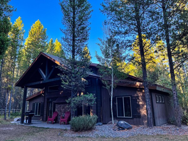 A cabin with a covered porch, two red Adirondack chairs, and a stone wall.