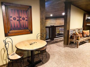 A cozy room with a round wooden table, two chairs, a bench with cushions, and a framed picture on the wall.