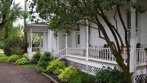 A white colonial-style house with a covered porch and a garden with various plants. - Granny's Farmhouse is a historic 1895 Victorian located on a working farm. (La Grande)