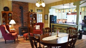 A cozy living room with a fireplace, a dining table with chairs, and a kitchen area with green cabinets and a refrigerator. - Granny's Farmhouse is a historic 1895 Victorian located on a working farm. (La Grande)