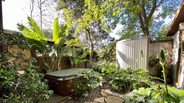 Un jardín con senderos de piedra, diversas plantas y una estructura de madera.