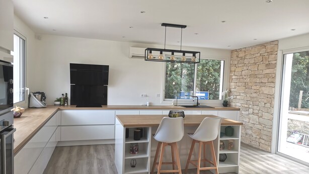 Una cocina moderna con una isla grande, armarios blancos y una pared de acento de piedra.
