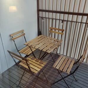 A small outdoor seating area with a metal table and chairs, a light fixture, and a metal fence.