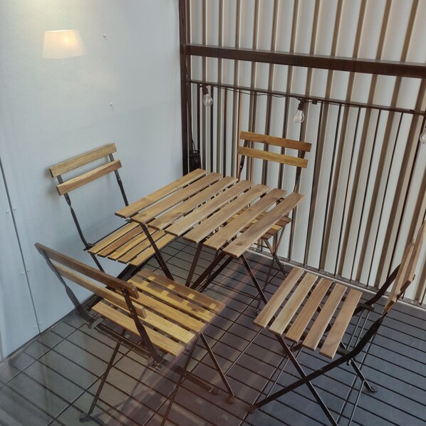 A small outdoor seating area with a metal table and chairs, a light fixture, and a metal fence.