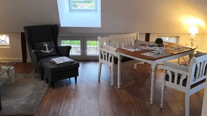 Une pièce spacieuse avec un plafond haut, une lucarne, une table à manger avec des chaises, un canapé et une petite table d’appoint.