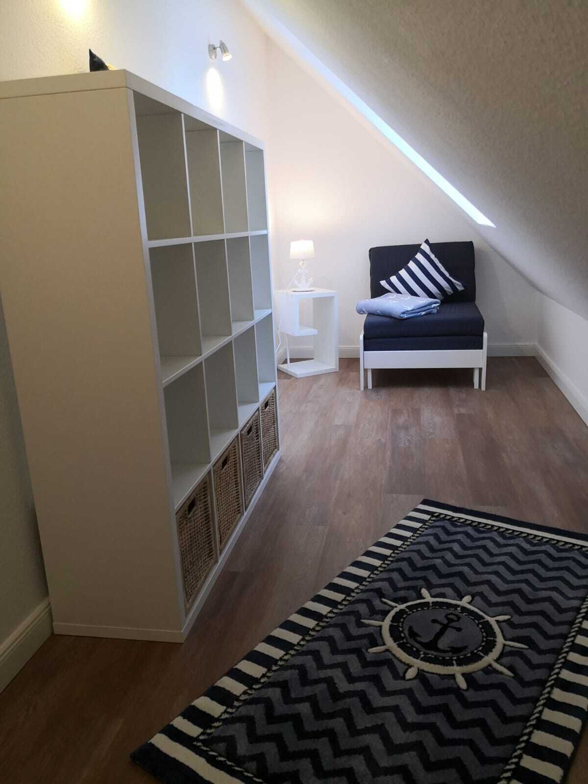 A room with a white wardrobe, a small white side table, a dark blue sofa with striped pillows, and a black and white chevron-patterned rug.