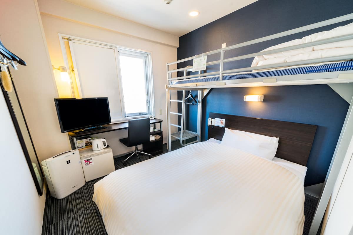A hotel room with a bunk bed, a desk with a computer, a television, a mini-fridge, and a mirror.