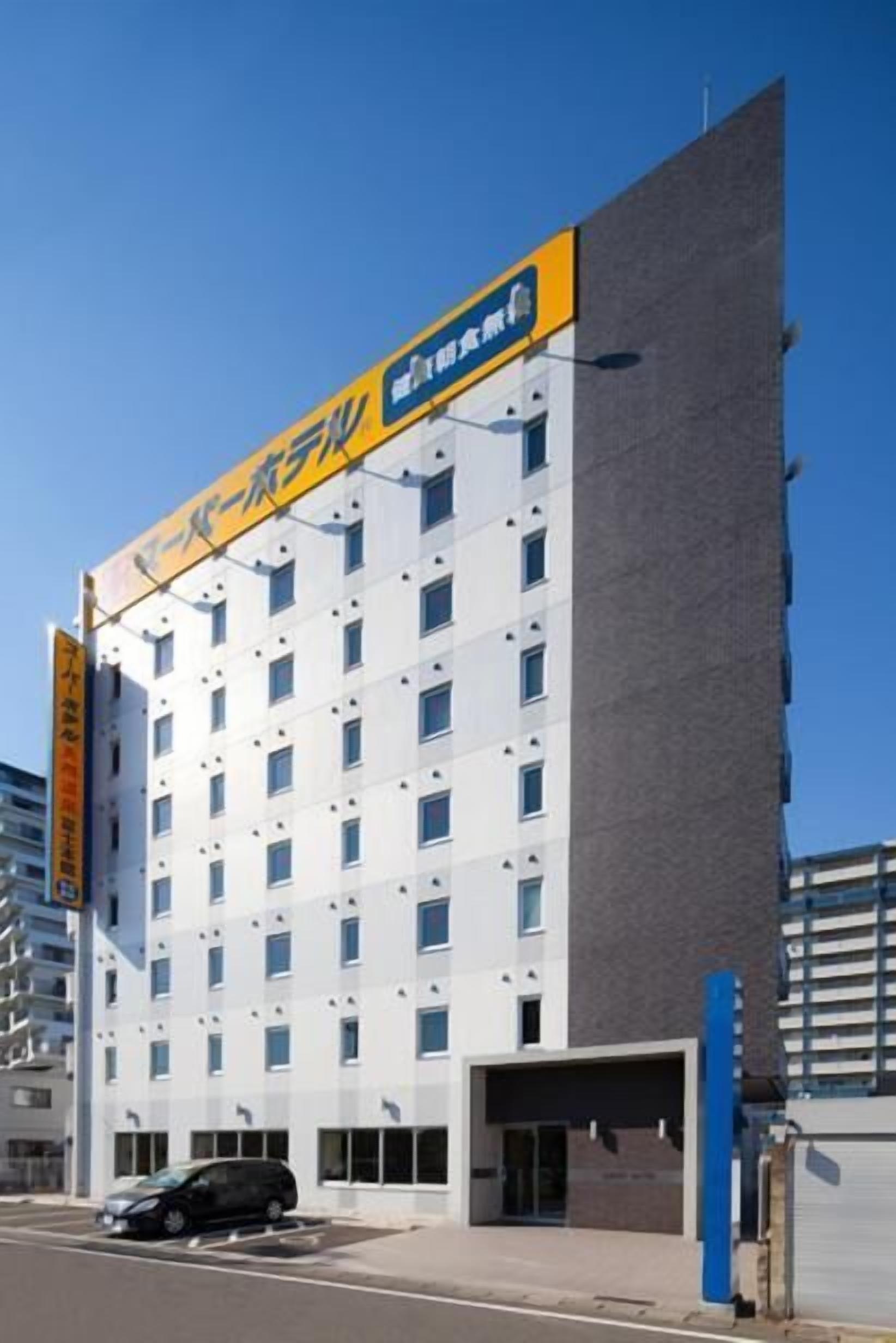 A modern hotel with a white facade and a yellow signboard.