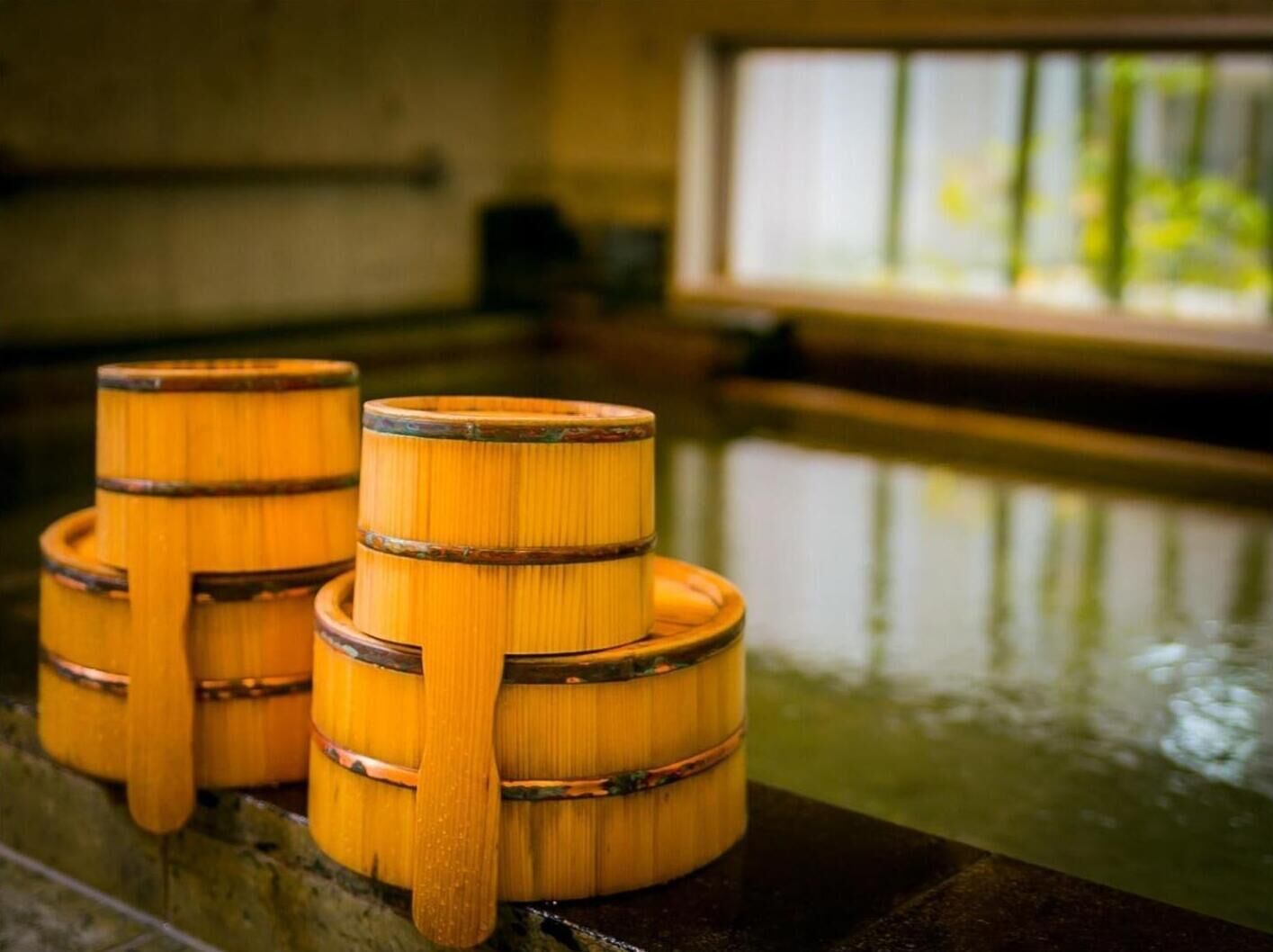 Trois barils en bois, empilés les uns sur les autres et dotés de poignées, sont placés sur une surface réfléchissante dans une pièce où l’on aperçoit une fenêtre au fond.