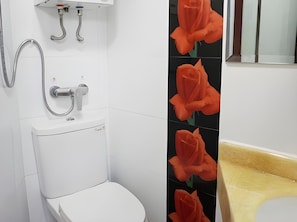 A bathroom with a white toilet, a shower with a chrome hose, and a sink with a beige countertop.