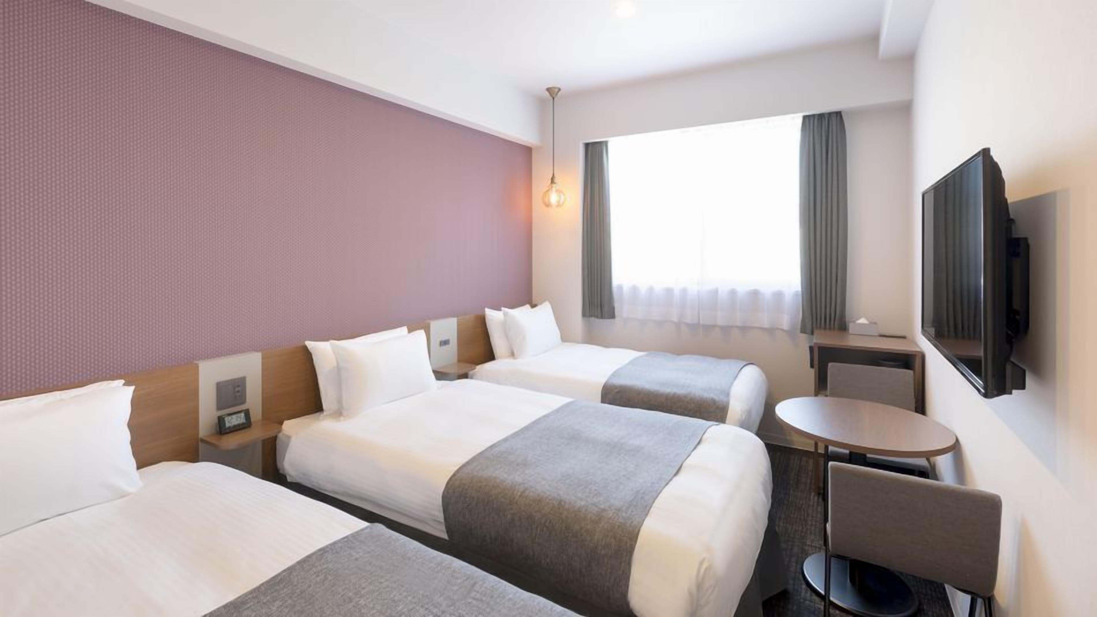 A hotel room with two beds, a desk, a chair, a TV, and a window with curtains.