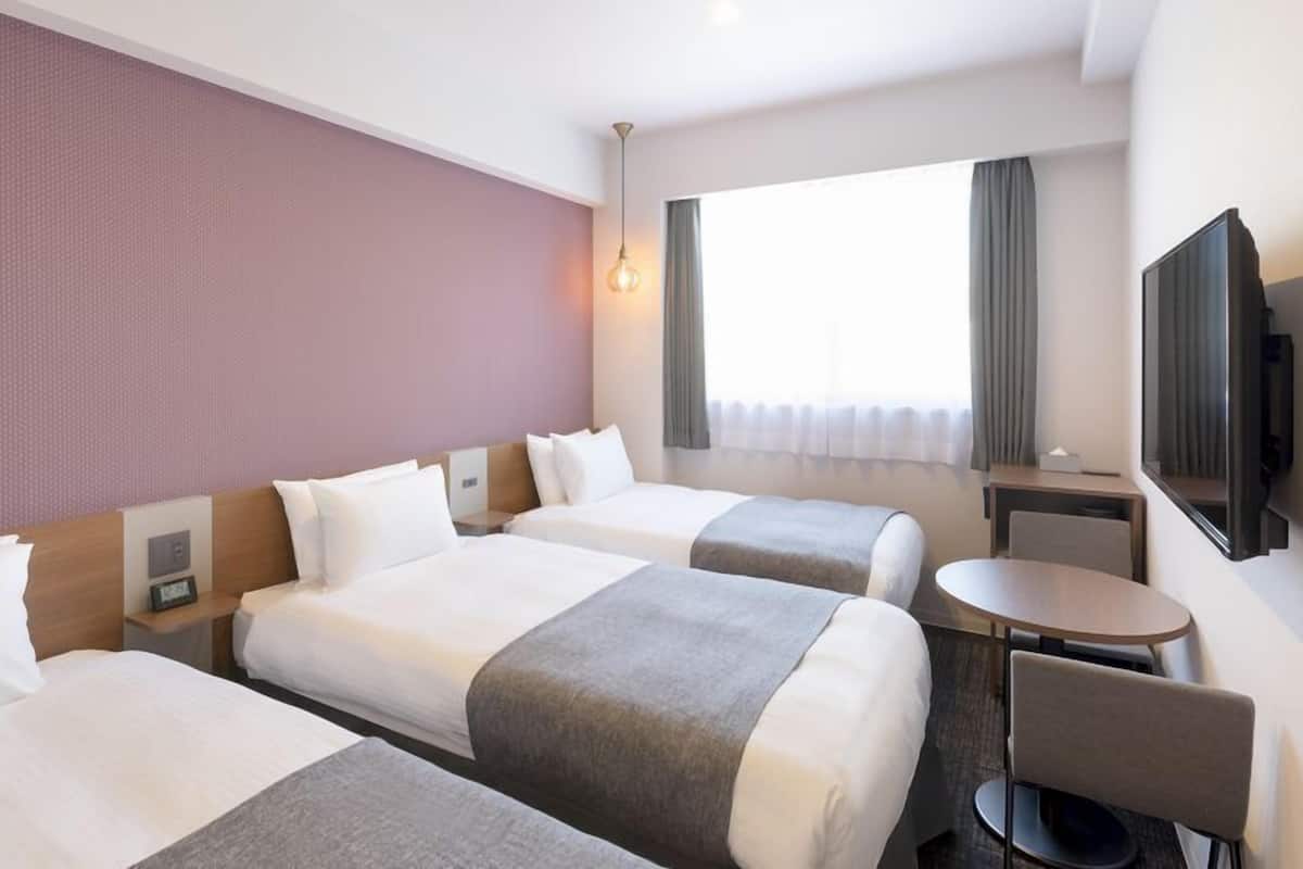 Quarto de hotel com duas camas, uma escrivaninha, uma cadeira, uma televisão e uma janela com cortinas.