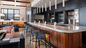 Un espace bar moderne avec un comptoir en bois, des tabourets de bar noirs et un éclairage suspendu.
