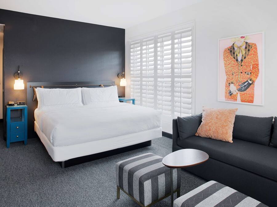 Una habitación de hotel moderna con una cama grande, un sofá, una mesita y una ventana con persianas.